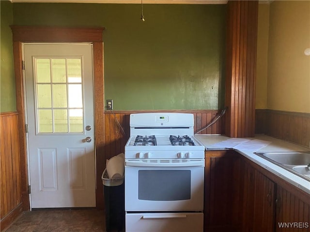 kitchen with a wainscoted wall, white gas stove, a sink, wooden walls, and light countertops