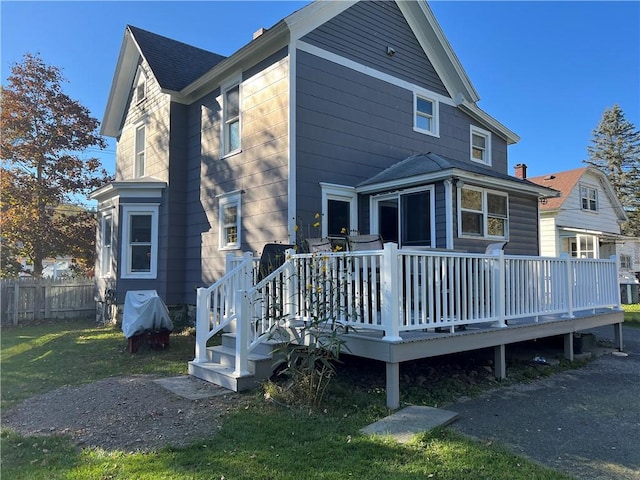 rear view of house with a deck, fence, a lawn, and a shingled roof