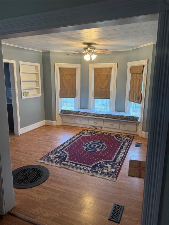 hall featuring visible vents, crown molding, baseboards, a wealth of natural light, and wood finished floors