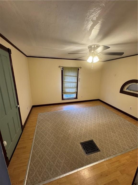 spare room with baseboards, visible vents, light wood finished floors, ceiling fan, and a textured ceiling