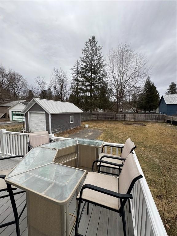 wooden terrace featuring an outdoor structure, outdoor dining area, a fenced backyard, and a lawn