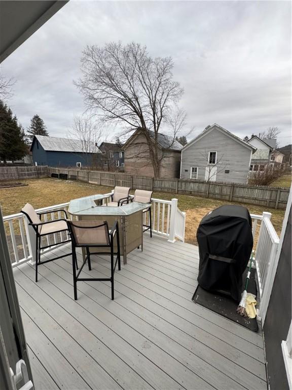 wooden terrace featuring a fenced backyard, outdoor dining space, a lawn, and grilling area