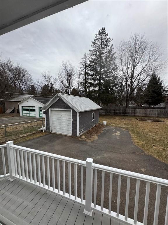 wooden deck with a garage, driveway, an outdoor structure, and fence