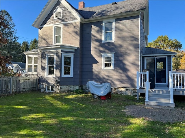 rear view of house featuring a deck, fence, a yard, roof with shingles, and a chimney