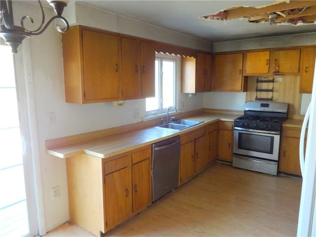 kitchen with a sink, appliances with stainless steel finishes, brown cabinetry, light wood finished floors, and light countertops