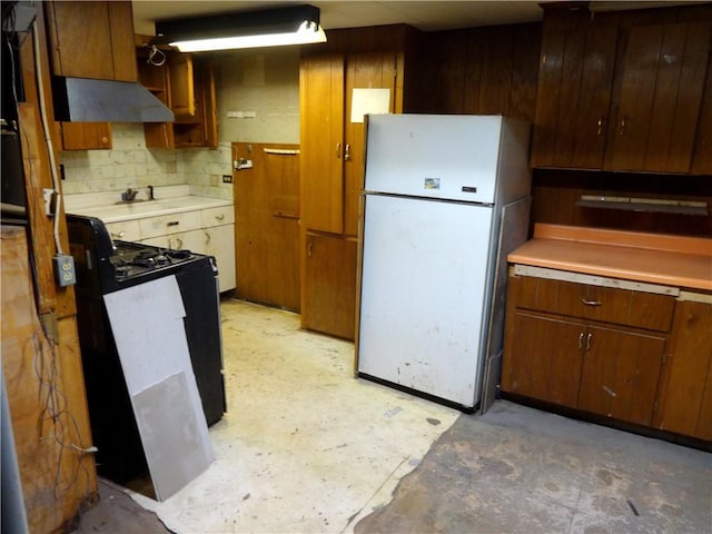 kitchen with under cabinet range hood, unfinished concrete flooring, light countertops, and freestanding refrigerator