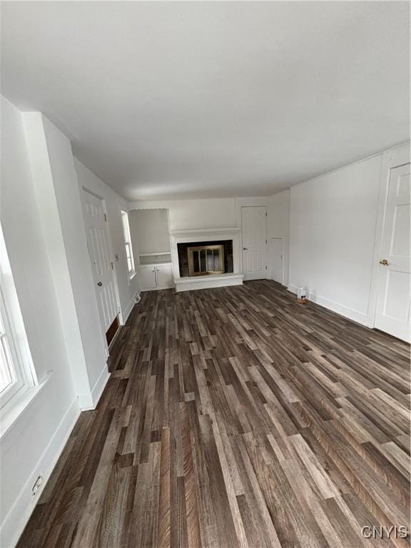 unfurnished living room with dark wood finished floors, a glass covered fireplace, and baseboards