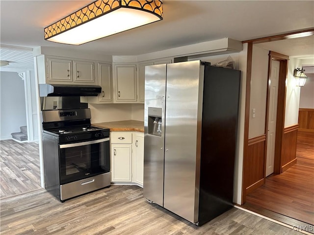 kitchen with under cabinet range hood, stainless steel appliances, a wainscoted wall, and light wood finished floors