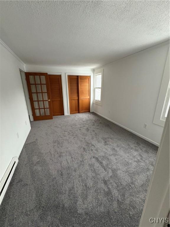 unfurnished bedroom with carpet, baseboards, baseboard heating, a textured ceiling, and two closets