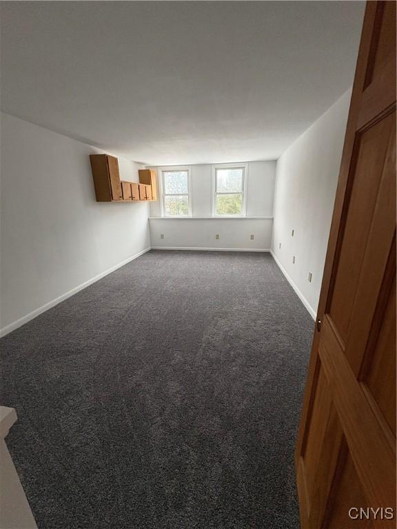 unfurnished room with baseboards and dark carpet