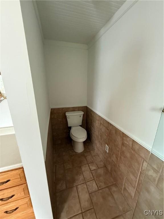 bathroom featuring tile patterned flooring, a wainscoted wall, toilet, and tile walls