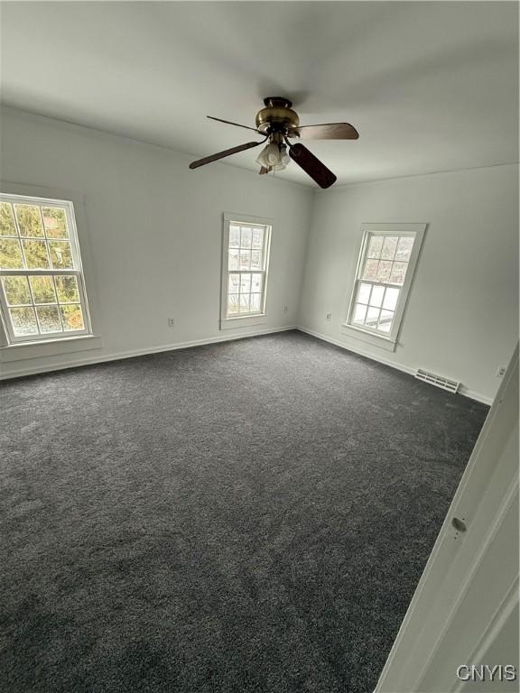 spare room featuring a wealth of natural light and dark colored carpet