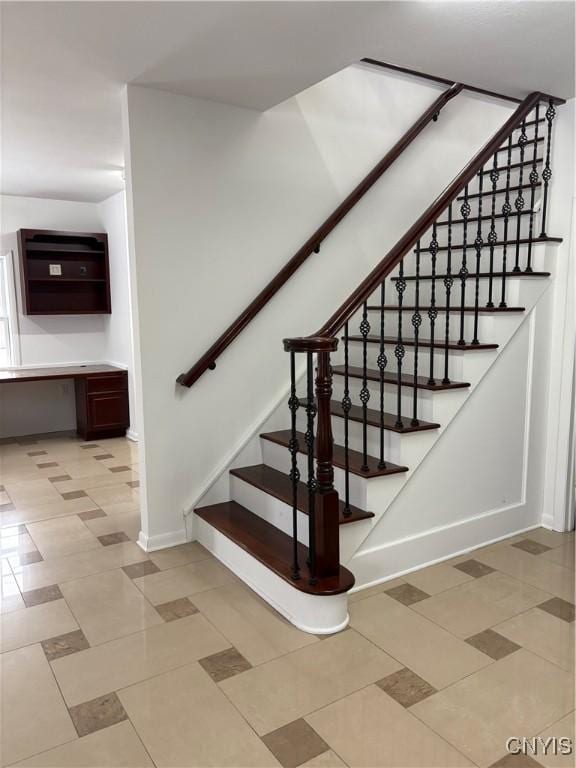 stairway featuring baseboards, built in study area, and tile patterned flooring