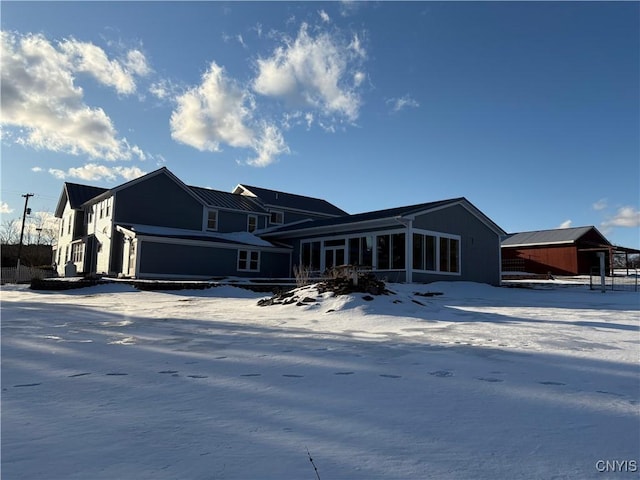 snow covered back of property featuring a sunroom