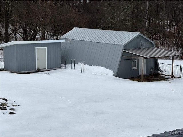 snow covered structure featuring an outbuilding and fence