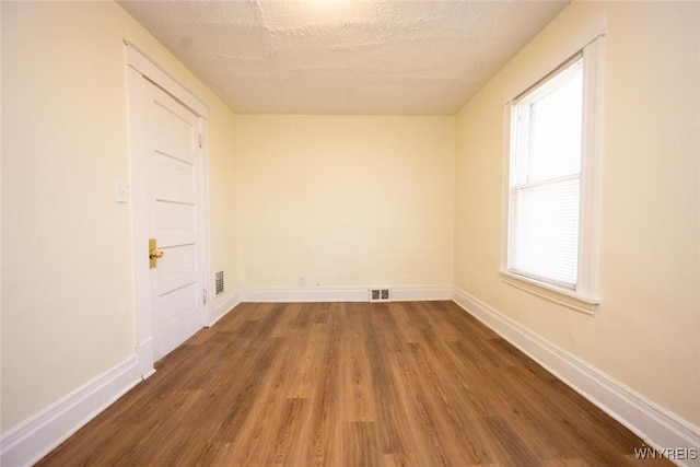 empty room featuring visible vents, baseboards, a textured ceiling, and wood finished floors