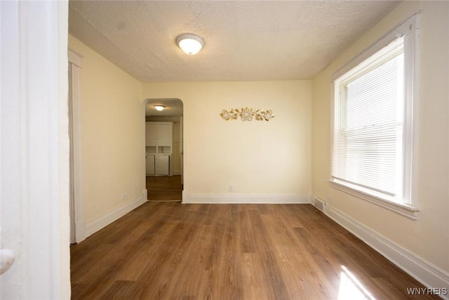 empty room featuring arched walkways, a textured ceiling, baseboards, and wood finished floors