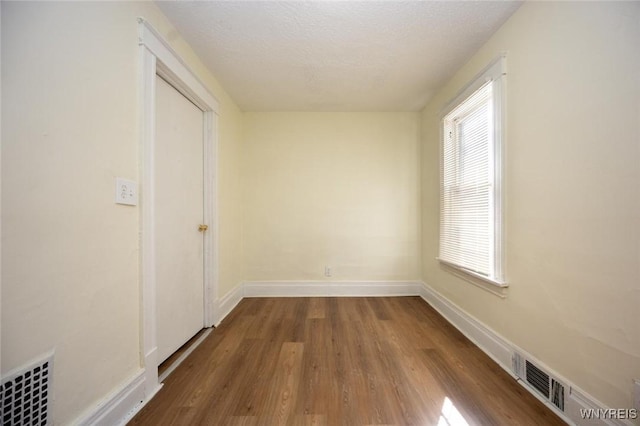 spare room with visible vents, a textured ceiling, baseboards, and wood finished floors