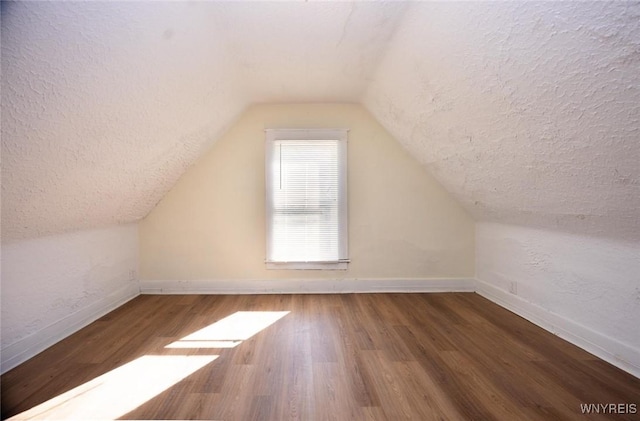 bonus room featuring vaulted ceiling, a textured ceiling, baseboards, and wood finished floors