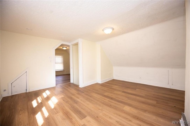 additional living space with vaulted ceiling, wood finished floors, baseboards, and a textured ceiling