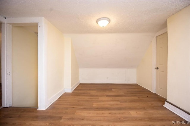 additional living space with baseboards, lofted ceiling, a textured ceiling, and wood finished floors