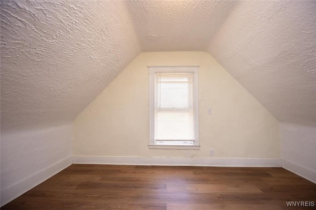 additional living space featuring baseboards, lofted ceiling, dark wood-type flooring, and a textured ceiling