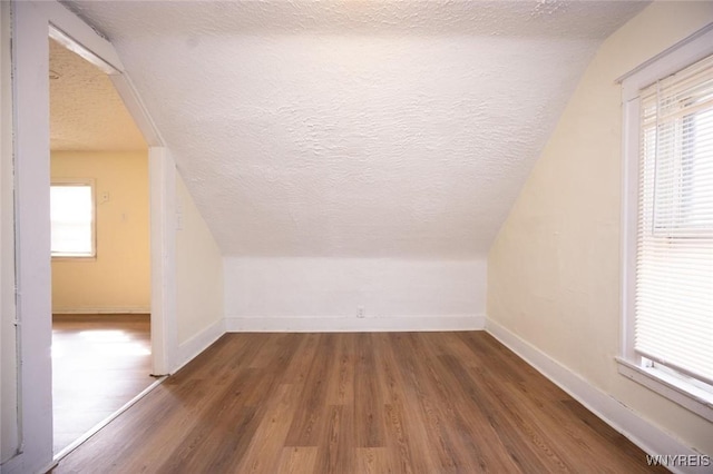 additional living space featuring lofted ceiling, wood finished floors, baseboards, and a textured ceiling