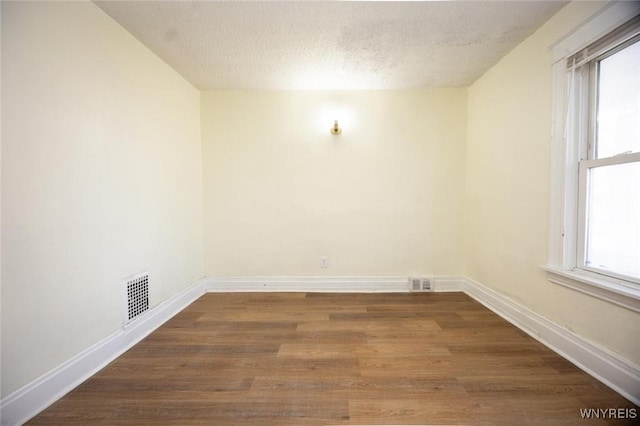 unfurnished room featuring visible vents, a textured ceiling, baseboards, and wood finished floors