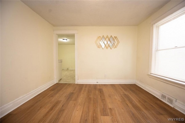 spare room with visible vents, baseboards, a textured ceiling, and wood finished floors