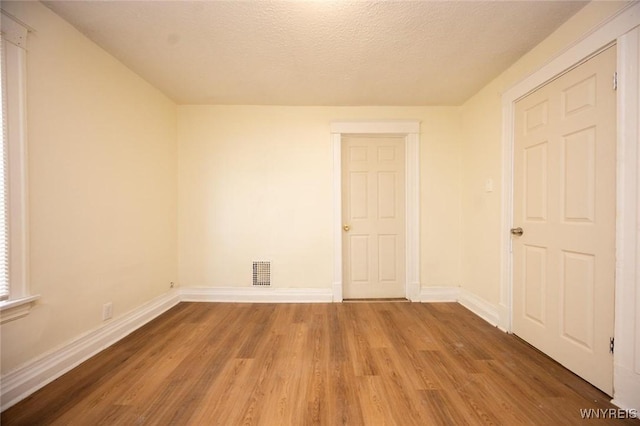 spare room with a textured ceiling, wood finished floors, visible vents, and baseboards