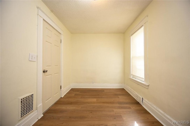 empty room featuring visible vents, baseboards, a textured ceiling, and wood finished floors