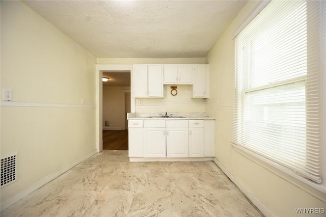 kitchen with visible vents, a sink, light countertops, white cabinets, and a textured ceiling