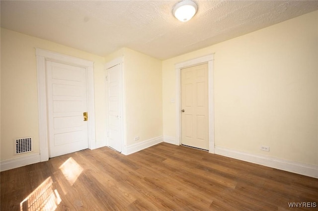 spare room featuring baseboards, wood finished floors, visible vents, and a textured ceiling