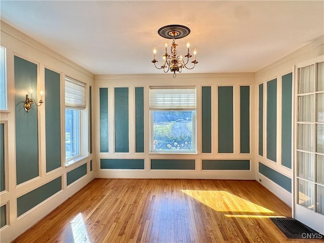 unfurnished dining area featuring an inviting chandelier, hardwood / wood-style floors, and a decorative wall