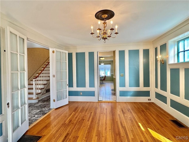 unfurnished room featuring visible vents, stairway, french doors, an inviting chandelier, and hardwood / wood-style flooring