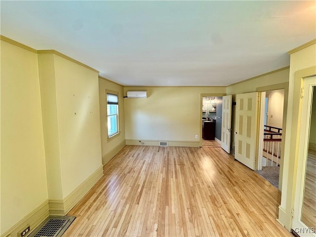 empty room with visible vents, light wood-style flooring, ornamental molding, a wall mounted AC, and baseboards