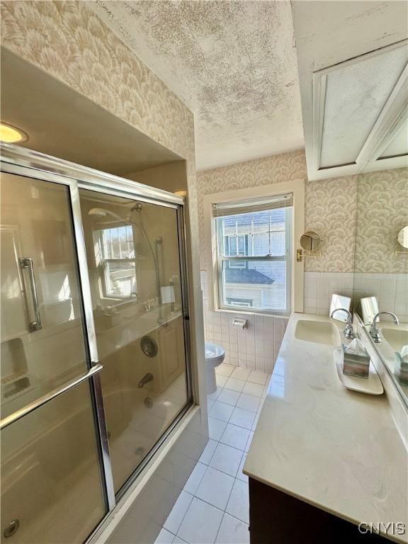 full bathroom featuring vanity, wallpapered walls, tile patterned flooring, a textured ceiling, and combined bath / shower with glass door