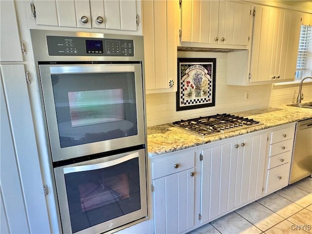 kitchen with backsplash, light stone countertops, white cabinets, stainless steel appliances, and a sink