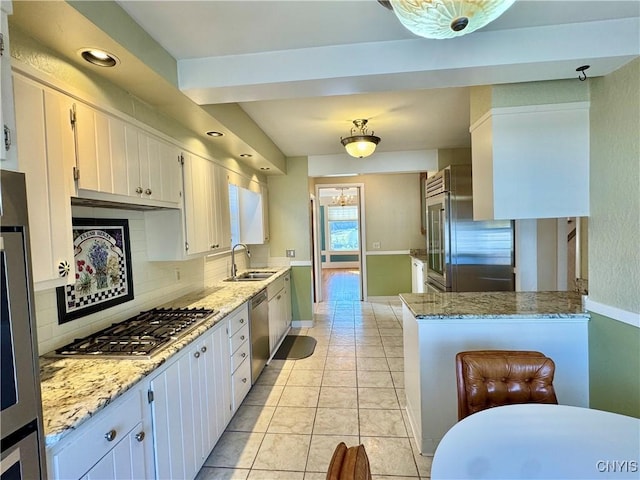 kitchen featuring backsplash, light stone counters, appliances with stainless steel finishes, light tile patterned flooring, and a sink