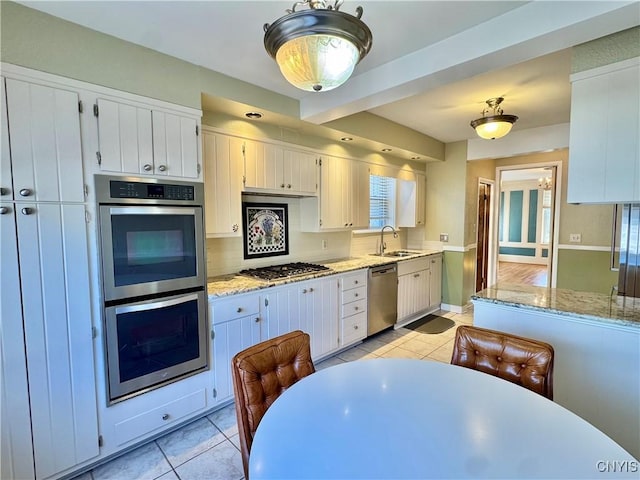 kitchen featuring light stone counters, light tile patterned floors, a sink, decorative backsplash, and appliances with stainless steel finishes