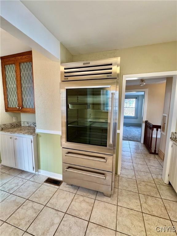 interior space with light stone counters, light tile patterned floors, glass insert cabinets, and wainscoting