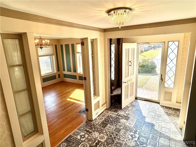 foyer featuring a notable chandelier, wood finished floors, a wealth of natural light, and ornamental molding