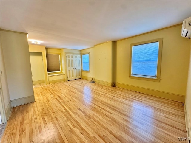 empty room featuring a wall unit AC, baseboards, light wood-style floors, and ornamental molding