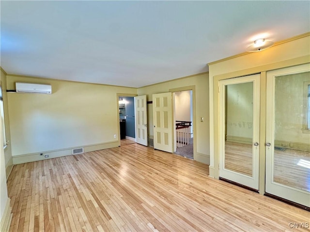 unfurnished room with visible vents, ornamental molding, a wall unit AC, and wood finished floors