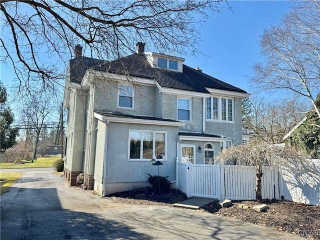 american foursquare style home with a fenced front yard, stucco siding, a chimney, and a gate