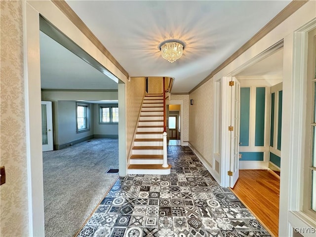 carpeted foyer featuring visible vents, wallpapered walls, crown molding, baseboards, and stairway