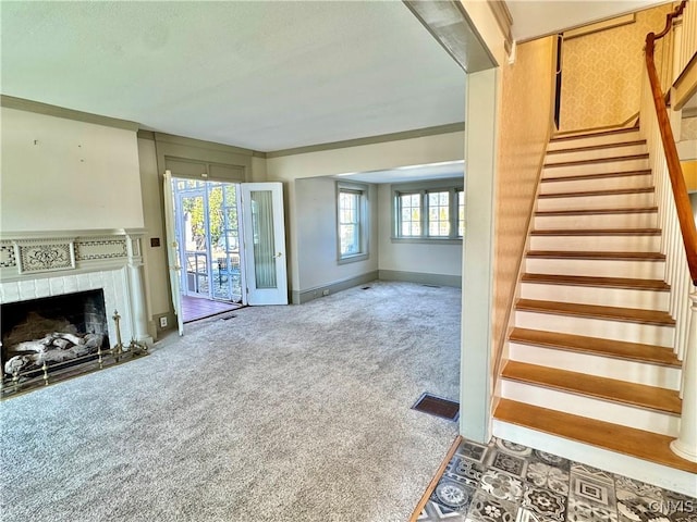 unfurnished living room with visible vents, a tiled fireplace, stairway, carpet, and baseboards