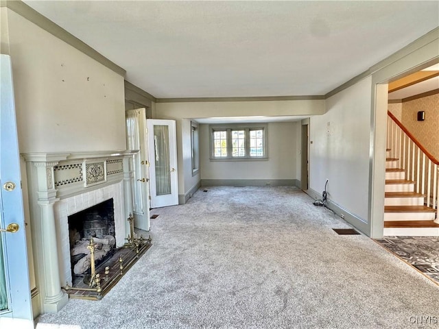 unfurnished living room featuring a fireplace with raised hearth, ornamental molding, carpet flooring, baseboards, and stairs