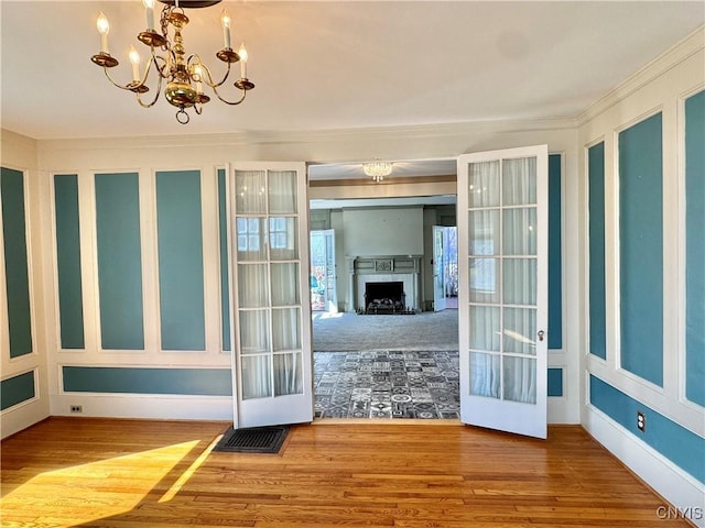 empty room with a chandelier, visible vents, a fireplace, and wood finished floors