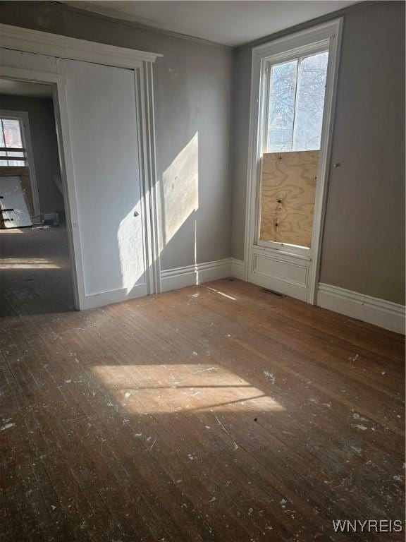 empty room with plenty of natural light, visible vents, baseboards, and wood-type flooring